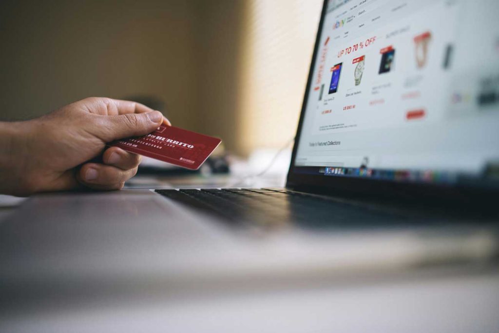 Hand holding a credit card is front of a computer showing an online store - e-Commerce in Cornwall